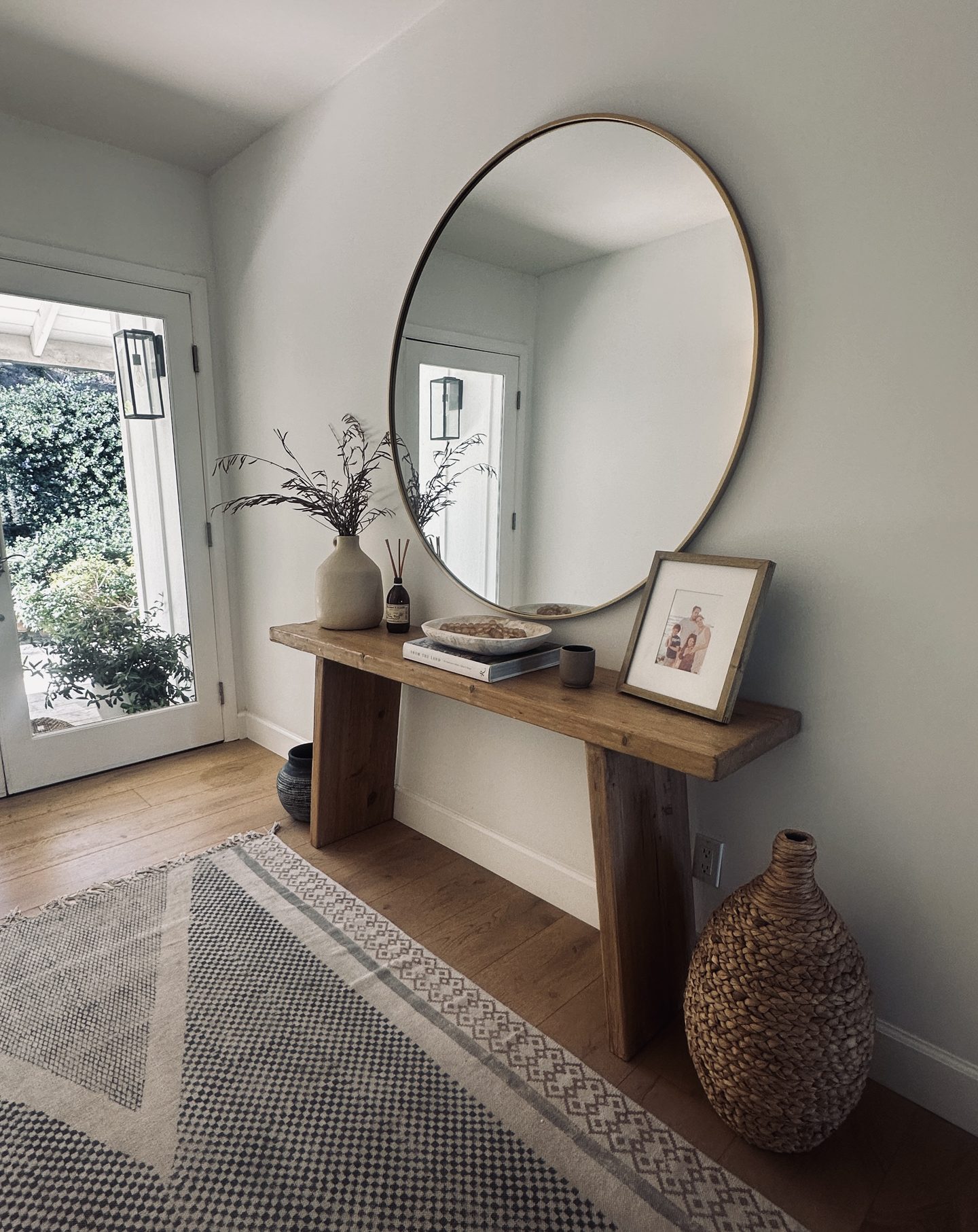 Styled entryway with a natural wood console, circular mirror, and woven floor vase